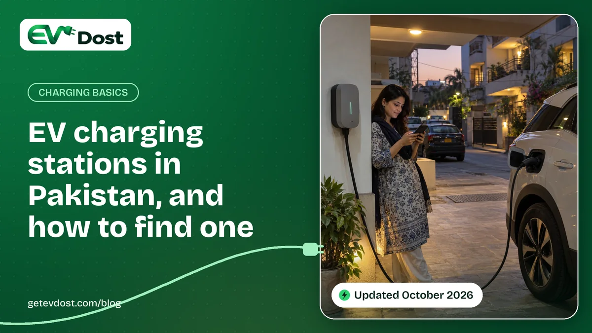 A woman checks her phone beside a wall-mounted charger connected to a white electric SUV on a city street at dusk
